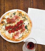 runde Pizza mit Käse, Tomaten und hauchdünnen Schinkenscheiben belegt