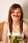 Frau mit langen Haaren hält rote Peperoni mit Nase und Mund