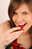 Portrait of woman with long hair eating strawberry, smiling, close-up