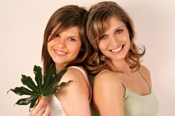 Portrait of two beautiful woman standing back to back with leaf in hand, smiling