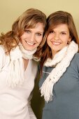 Portrait of two beautiful woman wearing sweater and scarf standing side by side, smiling