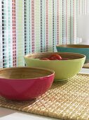 Three bowls in pink, green and blue colour on wicker mat