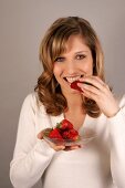 Portrait of beautiful woman biting into strawberry while holding plate of strawberries