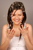 Close-up of pretty woman with brown hair cleaning her face with water, smiling