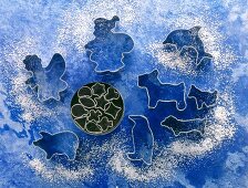 Various shaped cookie cutter with flour against blue background