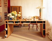 Schreibtisch aus Holz mit offenen Fächern rundum, Korbsessel, Blumen