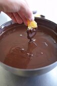Slice of orange being dipped in chocolate cream ganache