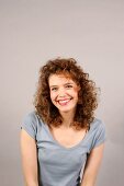 Portrait of beautiful woman with curly hair wearing gray top sitting and smiling widely
