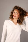 Beautiful woman with curly hair wearing white sweater standing with hand in hair, smiling