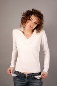 Beautiful woman with curly hair in white sweater and jeans showing her empty pockets