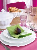 Table setting in pink and green with white plates and fig on top for decoration