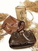 Three handbags in brown and beige between wood chips