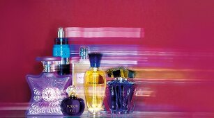 Diverse Parfüms in Flakons in Lila, Blau und Gelb, Hintergrund rot