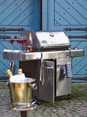 Large stainless steel grill with red champagne bottle and glasses in outdoors