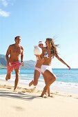 Two women and man playing with ball on the beach