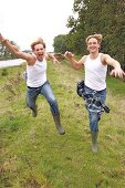 Two handsome men wearing white vest and jeans running on grass, smiling