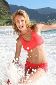 Portrait of happy blonde woman wearing red bikini playing in water
