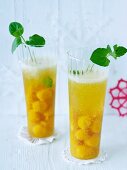 Two glasses of champagne with fruit puree balls and peppermint leaves
