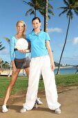 Two women playing ball under palm trees in a park