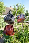 Three handbags in brown, black and red colour hanging on a wooden structure in garden