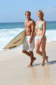 Mann und Frau gehen am Strand mit Surfbrett