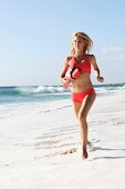 Sexy woman wearing swimsuit running on beach with a lifebuoy