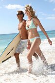Man and woman walking through waves with a surfboard