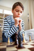 Junge in gestreiftem Pulli sitzt vor einem Schachbrett