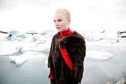 blonde Frau vor Eisschollen, trägt Pelzponcho, Blick nach links.X