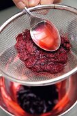 Cooked flower petals being strained in sieve while making geranium colour, step 4