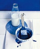 Schale mit blauer Wandfarbe und Pinsel, Milchflasche