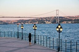 Rear view of woman standing near sea, overlooking city at sunset, Istanbul, Turkey