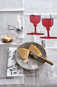 Newspaper spread as tablecloth with cheese, lit candle and two cup shaped cut out