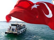 View of Turkish flag and people in transport ferry across Bosphorus, Istanbul, Turkey