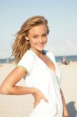 Portrait of young blonde woman wearing white zipper standing on beach, smiling