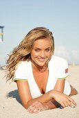 Portrait of pretty blonde woman wearing white zipper lying on beach, smiling
