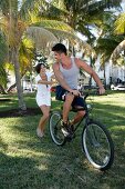 Man riding bicycle while woman pushing him, smiling and enjoying