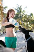 Red haired woman in casual outfit feeding water to dog, smiling