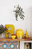 Yellow kitchen utensils such as vinegar pot and oil bottle on wooden shelf in Mediterranean kitchen