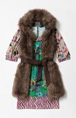 Fur vest with belt over colourful printed dress on white background