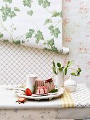 Vanille-Erdbeerparfait auf Tisch vor Wand dekoriert mit verschiedenen Tapetenrollen