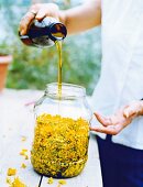 Close-up of woman pouring olive oil in glass jar with St. John's wort flowers