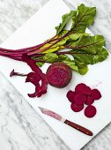Slices of beetroot and beetroot leaves on cutting board with knife, overhead view