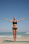 Woman wearing black bikini exercising on the beach, side view