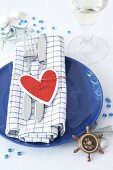 Name card holder in heart shape with knife, fork and napkin on blue plate