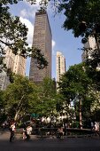 People relaxing in Madison Square Park overlooking skyscrapers, New York, USA