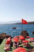 Turkish flag and people relaxing on sun loungers near sea in Antalya, Turkey