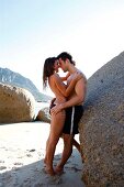 Seductive couple embracing each other and leaning against rock on beach