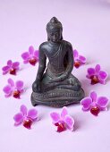 Statue of Buddha with orchid flowers on pink background