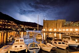 Boats moored on Dubrovnik old harbour with thunderstorm at night in Croatia